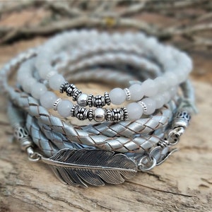 May include: A multi-strand bracelet with a silver feather charm. The bracelet is made of braided leather and features white beads and silver accents.