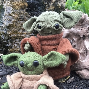 May include: Two knitted green and brown plush toys resembling a popular fictional character. The larger toy is wearing a brown sweater and the smaller toy is wearing a tan sweater.