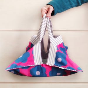 Può includere: Una borsa tote floreale rosa e blu con manici a righe bianche e grigie. La borsa è realizzata in tessuto e ha una parte superiore larga e aperta.