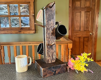 May include: A rustic wooden mug rack shaped like a tree with four hooks. The rack is stained dark brown and has a natural wood grain. There are four mugs hanging on the hooks, two black and two white. The rack is sitting on a dark brown countertop. The text "Boss Babe" is visible on one of the white mugs.