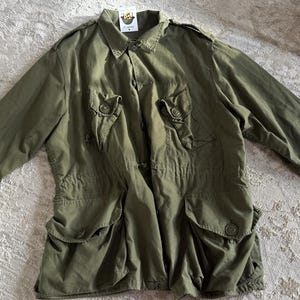 Puede incluir: Una chaqueta utilitaria verde con múltiples bolsillos y cierre de botones.