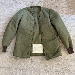 May include: A green quilted jacket with a snap closure and a label on the front. The label has text that reads "U.S. ARMY"