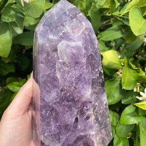 May include: A large, purple amethyst crystal point with a faceted, geometric shape. The crystal has a natural, rough texture and is a deep, rich purple color.