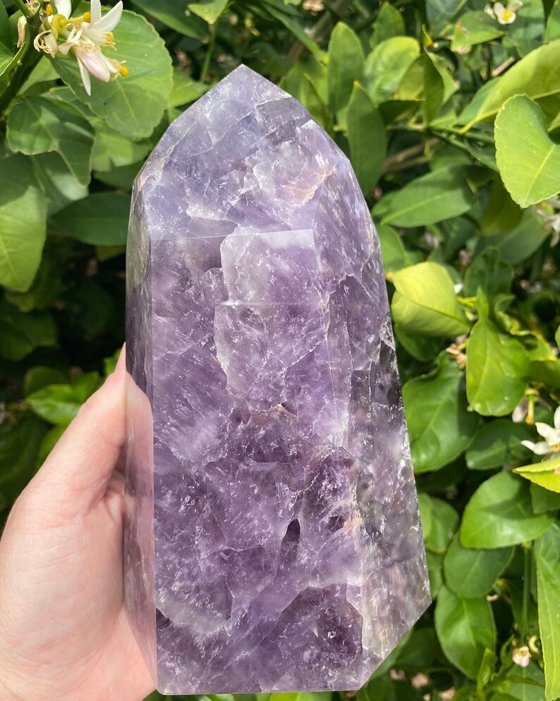 May include: A large, purple amethyst crystal point with a faceted, geometric shape. The crystal has a natural, rough texture and is a deep, rich purple color.