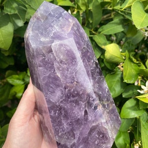 May include: A large, purple amethyst crystal point with a faceted, geometric shape. The crystal is smooth and polished, with a deep purple hue.