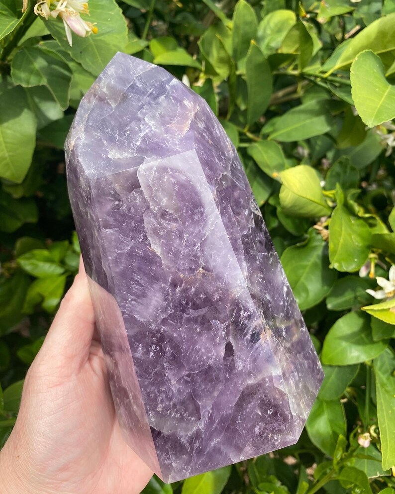 May include: A large, purple amethyst crystal point with a faceted, geometric shape. The crystal is smooth and polished, with a deep purple hue.