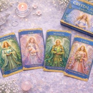 Op de afbeelding: Een set Crystal Angel Tarotkaarten met vier kaarten afgebeeld, met engelenillustraties en titels als "Emerald Raphael" en "Opal". De kaarten liggen op een lichtpaarse ondergrond met bloemen en kristallen, naast een doosje kaarten.