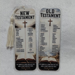 Puede incluir: Dos marcadores religiosos con borlas. Uno dice "NUEVO TESTAMENTO" y el otro "ANTIGUO TESTAMENTO". Cada marcador presenta una cruz, una lista de libros y la cita "Tu palabra es una lámpara a mis pies, y una luz en mi camino. Salmo 119:105."