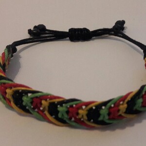 Peut inclure: Bracelet tressé avec un motif de fils rouges, jaunes, verts et noirs. Le bracelet est doté d'une fermeture réglable en cordon noir. Le design tressé donne un aspect texturé, adapté au quotidien.