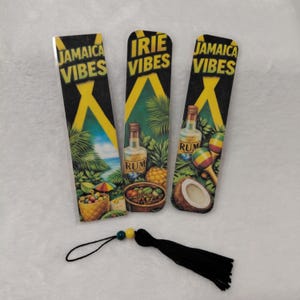 May include: Three rectangular bookmarks with a black background and yellow accents. The bookmarks feature the text "Jamaica Vibes" and "Irie Vibes". Each bookmark has a different tropical scene with a bottle of rum, fruit, and maracas. A black tassel is attached.