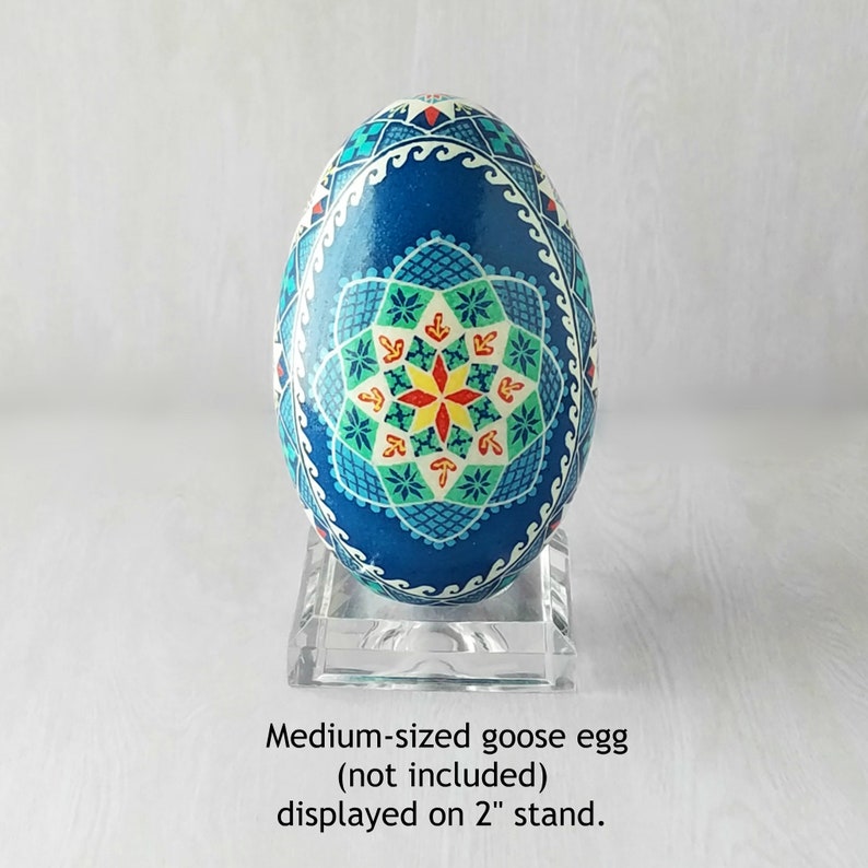 May include: A blue goose egg with a white, red, and yellow geometric design is displayed on a clear acrylic stand. The egg is approximately 2 inches in diameter.