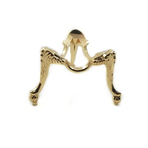 May include: Gold metal egg stand with three ornate legs. The stand is designed to hold a single egg.