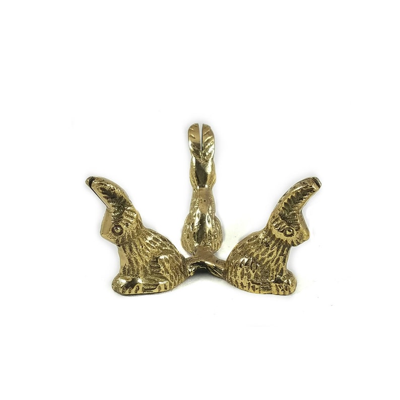 May include: Gold-toned metal decorative stand shaped like three rabbits sitting back to back. The stand has a round top and is designed to hold small items.