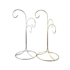 May include: Two metal ornament display stands. One is silver, the other is gold. Each stand has a circular base and a curved top with hooks for hanging ornaments. The stands are designed to hold multiple ornaments.