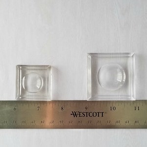 May include: Two clear glass display domes, one smaller than the other, are shown on a white surface with a ruler underneath. The ruler is marked with inches and fractions of an inch. The smaller dome is about 6 inches wide and the larger dome is about 9 inches wide.