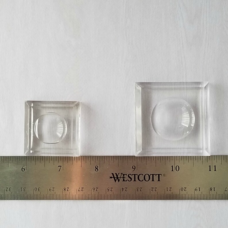 May include: Two clear glass display domes, one smaller than the other, are shown on a white surface with a ruler underneath. The ruler is marked with inches and fractions of an inch. The smaller dome is about 6 inches wide and the larger dome is about 9 inches wide.