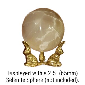 May include: Gold metal stand with three rabbit-shaped legs, designed to hold a sphere. The stand is displayed with a 2.5 inch (65mm) selenite sphere, which is not included.