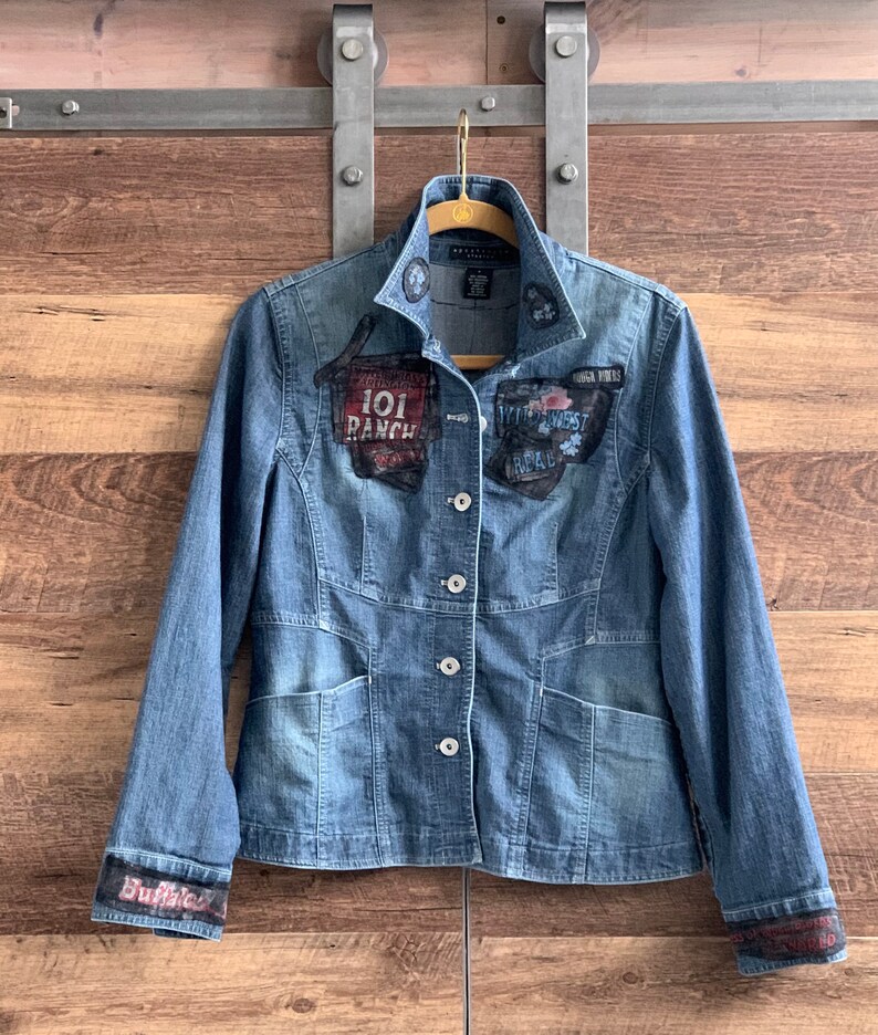 May include: A blue denim jacket with several patches, including "101 Ranch" and "Wild West Road", on the front. The jacket has a button closure and two pockets.