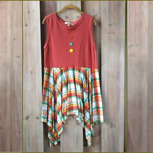 Pu&ograve; includere: Un abito rosso in cotone senza maniche con una gonna a quadri. L'abito ha un collo alto e quattro bottoni colorati sul davanti. La gonna &egrave; un mix di quadri rossi, arancioni, verdi e bianchi.