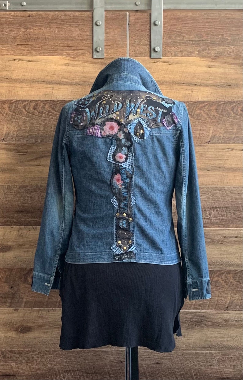 May include: A blue denim jacket with a floral and patchwork design on the back. The design includes the words "Wild West" in a gold and black font.