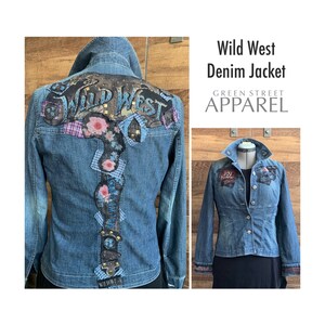 May include: A blue denim jacket with a patchwork design on the back. The back features the words "Wild West" in a distressed font. The jacket has a button closure and two pockets on the front. The jacket is from Green Street Apparel.