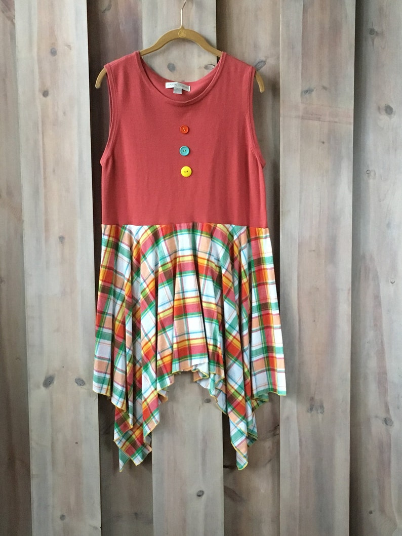 Pu&ograve; includere: Un vestito senza maniche con una parte superiore rossa e una gonna a quadri. La gonna &egrave; un mix di quadri bianchi, arancioni, verdi e rossi. La parte superiore ha quattro bottoni sul davanti, uno rosso, uno blu, uno verde e uno giallo.