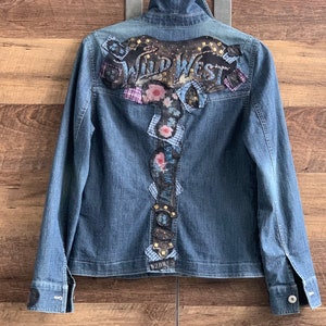 May include: A blue denim jacket with a large embroidered patch on the back that says "Wild West" with floral and geometric designs.