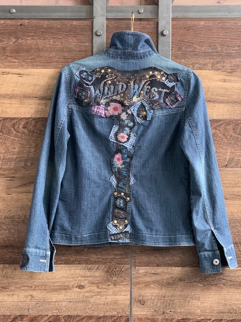 May include: A blue denim jacket with a large embroidered patch on the back that says "Wild West" with floral and geometric designs.