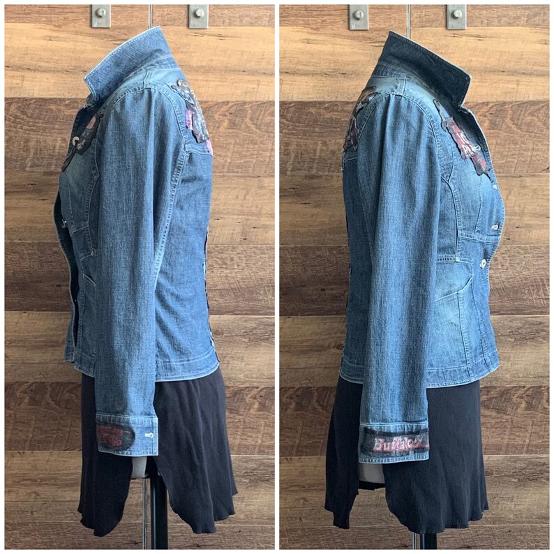 May include: A blue denim jacket with a variety of colorful patches and embellishments. The jacket has a button-up front and long sleeves. The cuffs of the sleeves have a black and white patterned fabric with the word "Buffalo" printed on them.