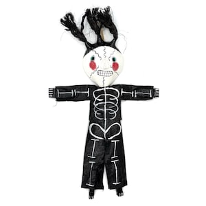 May include: A black and white skeleton doll with red cheeks and black hair. The doll is wearing a black outfit with a white skeleton design.