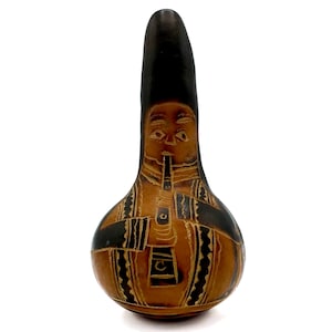 Può includere: Un'opera d'arte artigianale in zucca raffigurante un musicista che suona il flauto. La zucca è marrone con disegni incisi marrone scuro e neri. Il volto e gli abiti del musicista sono intagliati in modo intricato.