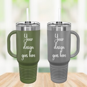 Puede incluir: Dos tazas de viaje de acero inoxidable con asas y tapas. La taza de la izquierda es verde y la taza de la derecha es gris. Ambas tazas tienen una pajita y el texto "Your design goes here" impreso en el lateral.