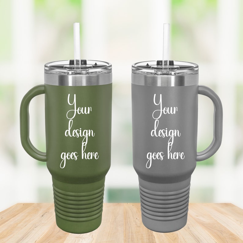 Puede incluir: Dos tazas de viaje de acero inoxidable con asas y tapas. La taza de la izquierda es verde y la taza de la derecha es gris. Ambas tazas tienen una pajita y el texto "Your design goes here" impreso en el lateral.