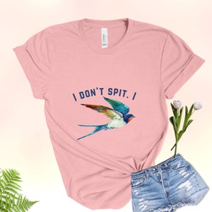 Puede incluir: Una camiseta rosa con el texto "I DON'T SPIT. I" y una ilustraci&oacute;n de golondrina colorida.