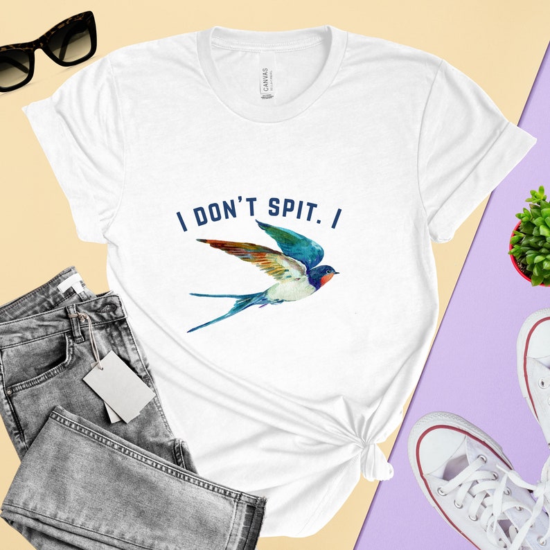 Puede incluir: Camiseta blanca con un gr&aacute;fico de golondrina azul y el texto "I DON'T SPIT. I" impreso en la parte delantera.