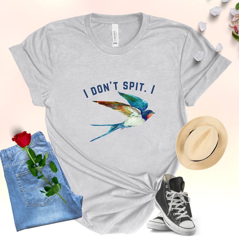 Puede incluir: Una camiseta gris claro con un gr&aacute;fico de golondrina azul y el texto "I DON'T SPIT. I" impreso en la parte delantera.