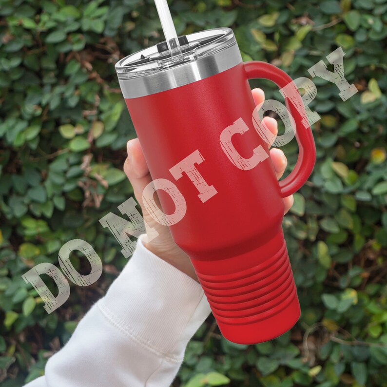 Puede incluir: Taza de viaje de acero inoxidable roja con asa y tapa. La taza tiene un fondo texturizado y una pajita.