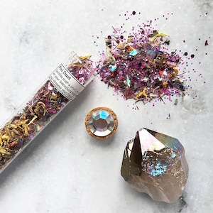 May include: A glass tube filled with colorful glitter and dried flowers, labeled "Pixi Dust Sprinkle over a candle, set your intentions and let your dreams manifest!"