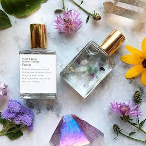 May include: A clear glass bottle with a gold cap and a white label that reads "Violet & Poppy Sensory Therapy Focus Fluorite enhances mental clarity and increases focus. Brings a wiser, more balanced view, improving decision making."