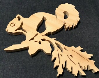 May include: A wooden cutout of a squirrel sitting on a branch with acorns. The squirrel is facing left and has a bushy tail. The branch has leaves and acorns.