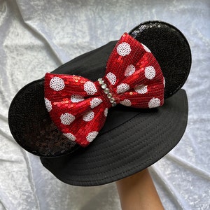 May include: Black bucket hat with a red and white polka dot bow and black sequined ears.