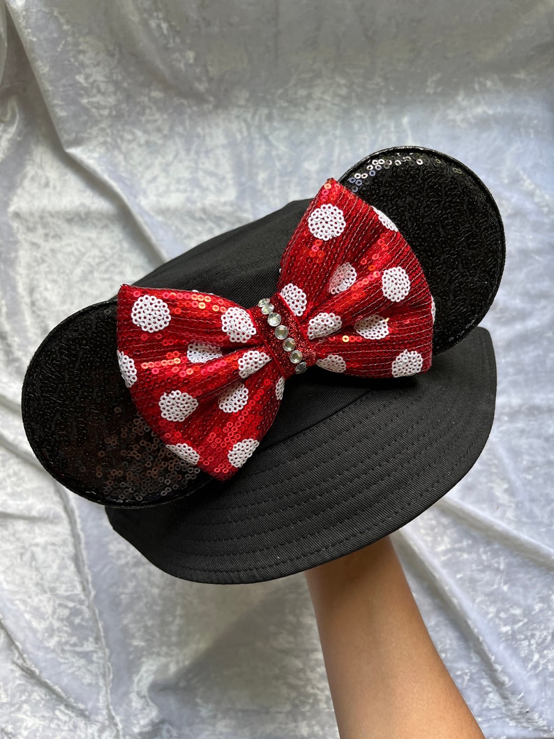 May include: Black bucket hat with a red and white polka dot bow and black sequined ears.