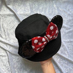 May include: Black bucket hat with a red and white polka dot bow and black sequin ears.