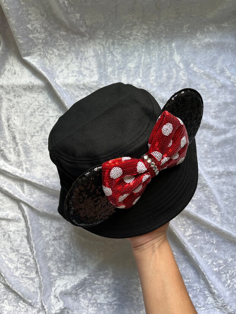 May include: Black bucket hat with a red and white polka dot bow and black sequin ears.