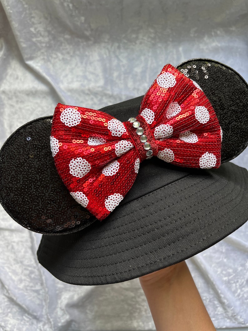 May include: Black bucket hat with a red and white polka dot bow and black sequined mouse ears.