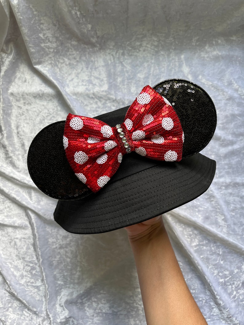 May include: Black bucket hat with a red and white polka dot bow and black sequin ears.