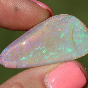 May include: A teardrop-shaped opal gemstone featuring a translucent white base with vibrant flashes of green, blue, and pink iridescence throughout the surface. The stone displays a smooth, polished finish and a distinct curved internal inclusion line.