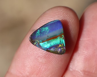 May include: A triangular opal gemstone with a vibrant display of colors. The stone features a mix of blues, greens, and hints of red and gold. The polished surface reflects light, showcasing the play-of-color effect.