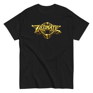 Könnte beinhalten: Ein schwarzes Kurzarm-T-Shirt mit einer metallisch goldenen Grafik auf der Brust. Die Grafik zeigt das Wort ULTIMATE in einer fetten, stilisierten Schrift mit dreidimensionaler Optik, umgeben von scharfen, winkligen, flügelartigen Formen.