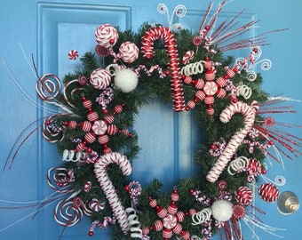 May include: A Christmas wreath decorated with candy canes, peppermint swirls, and red and white ornaments. The wreath is on a blue door.